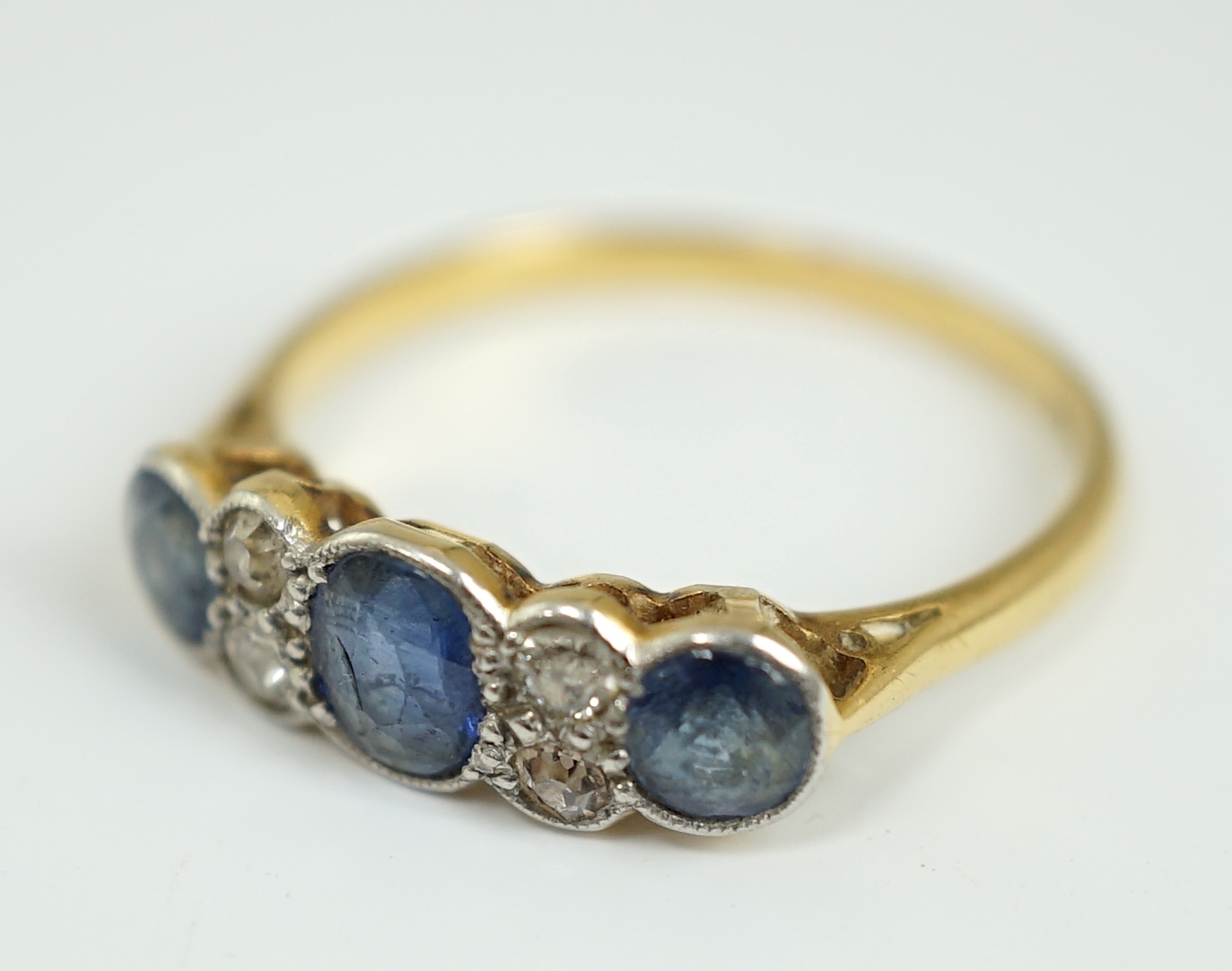 A 1920's 18ct gold and platinum, millegrain set three stone sapphire and four stone diamond half hoop ring